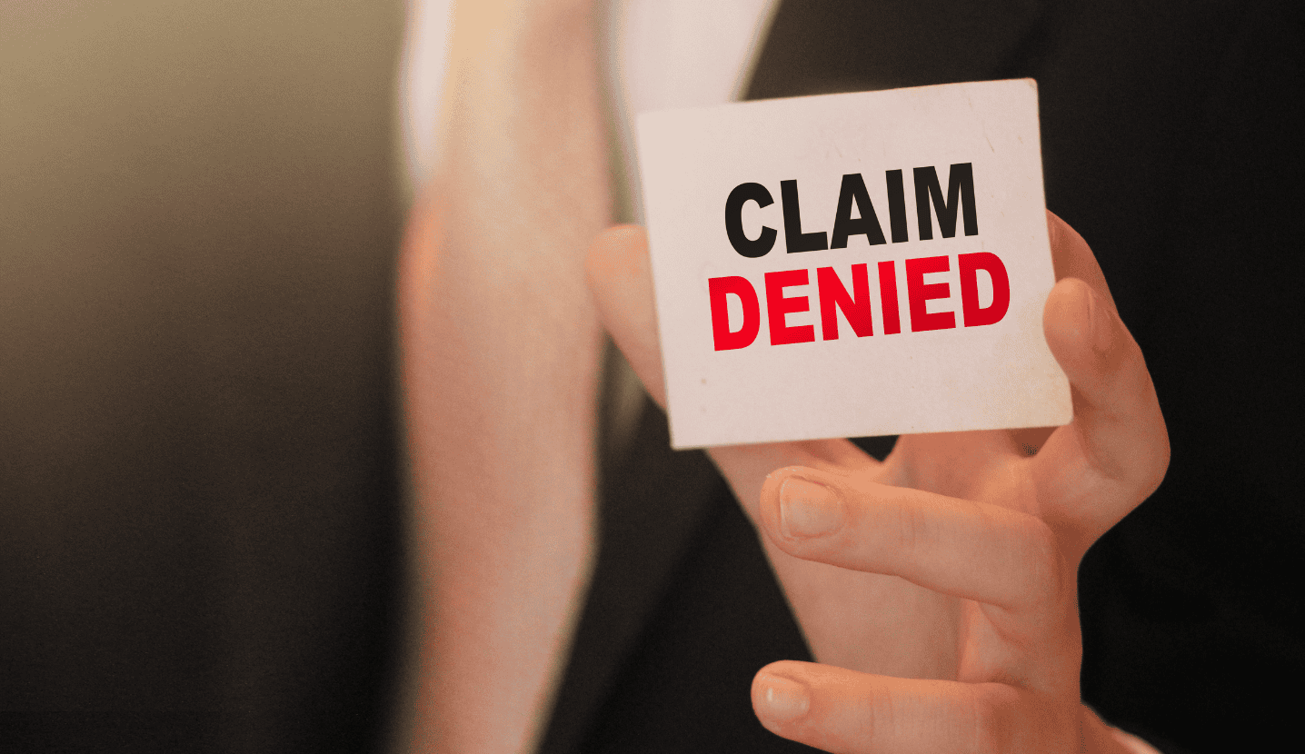 Person in a black suit holding a note card that reads, "claim denied".