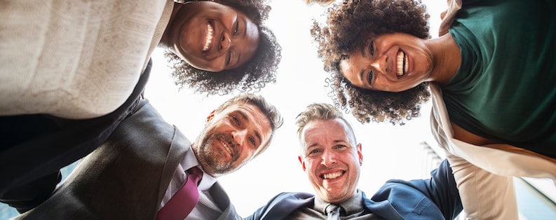 Two men and two women in office attire huddled in a circle smiling before.