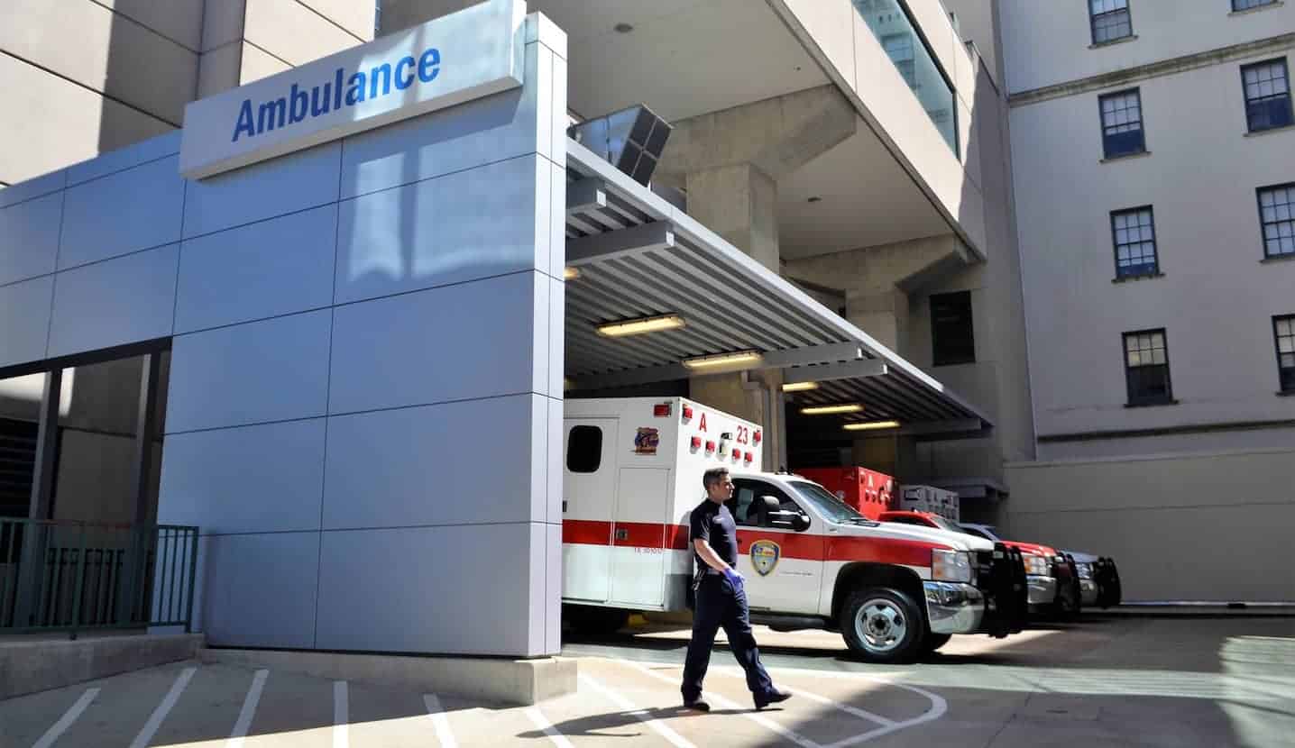 Emergency first responder walks in a hospital parking lot in front of an ambulance.